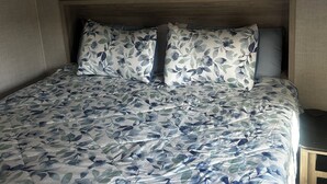 Une chambre à coucher avec un lit, une literie à motifs floraux, une tête de lit en bois et des armoires encastrées.