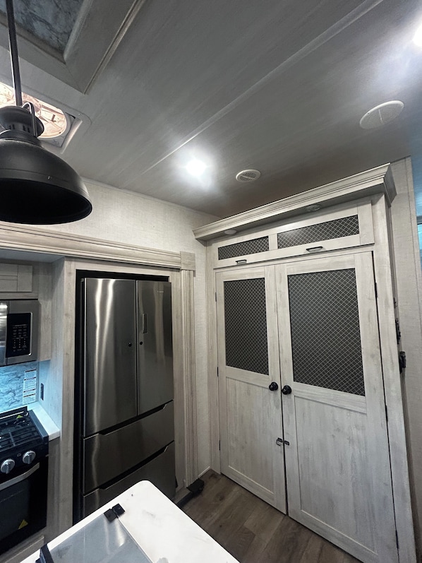 A kitchen with stainless steel appliances, white cabinetry, and a pendant light. - Cozy Camper on a mini farm with marsh front views! (Yulee)
