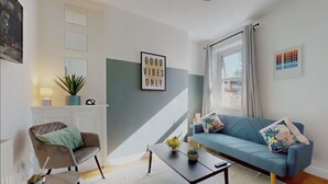 A modern living room with a blue sofa, a small coffee table, and a chair. There is a fireplace, a plant, and a wall with a motivational quote. - Two Bedroom House in Cardiff City (Cardiff)