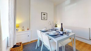 A dining area with a table set for two, a bottle of wine, and a vase with flowers. - Two Bedroom House in Cardiff City (Cardiff)