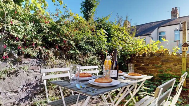 An outdoor dining table with plates of food, a bottle of wine, and glasses. - Two Bedroom House in Cardiff City (Cardiff)