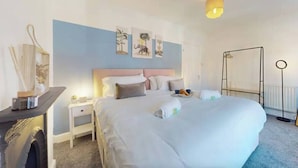 A neatly arranged hotel room with a large bed, bedside tables, a nightstand, a lamp, and artwork on the wall. - Two Bedroom House in Cardiff City (Cardiff)