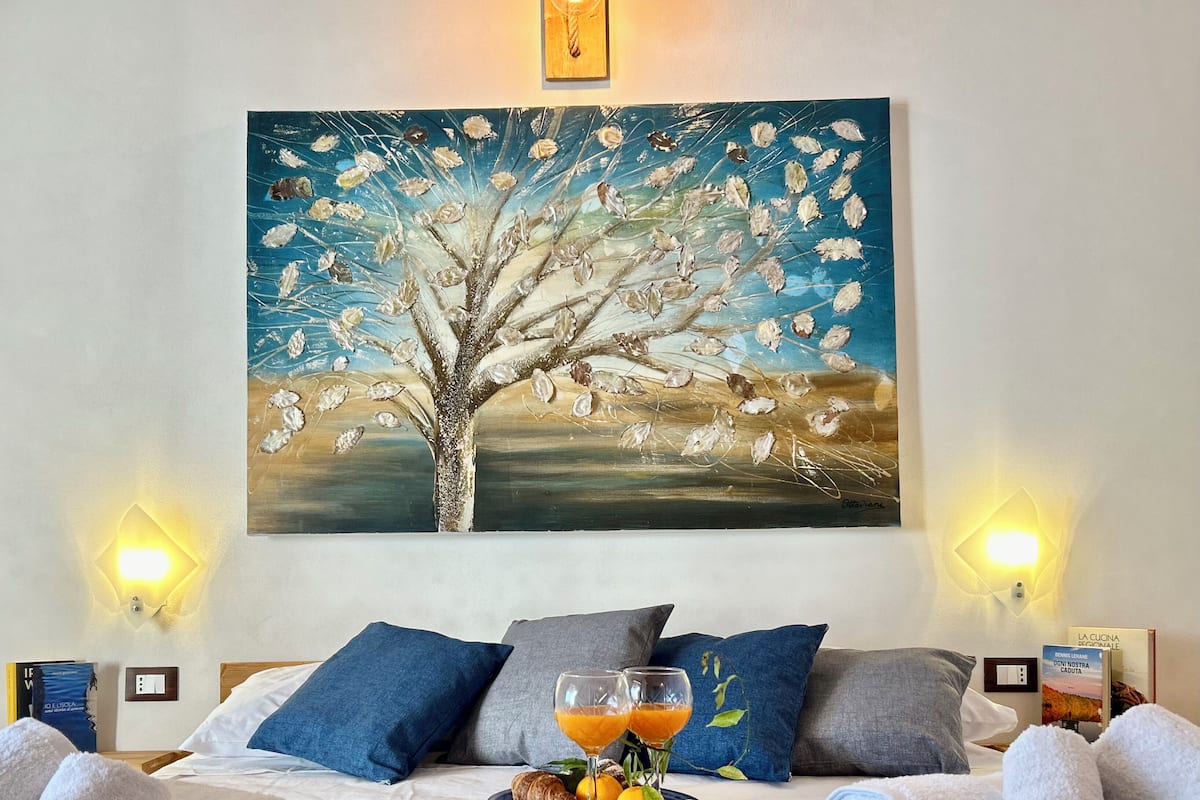 A hotel room with a bed, pillows, a painting, a glass of orange juice, and towels.