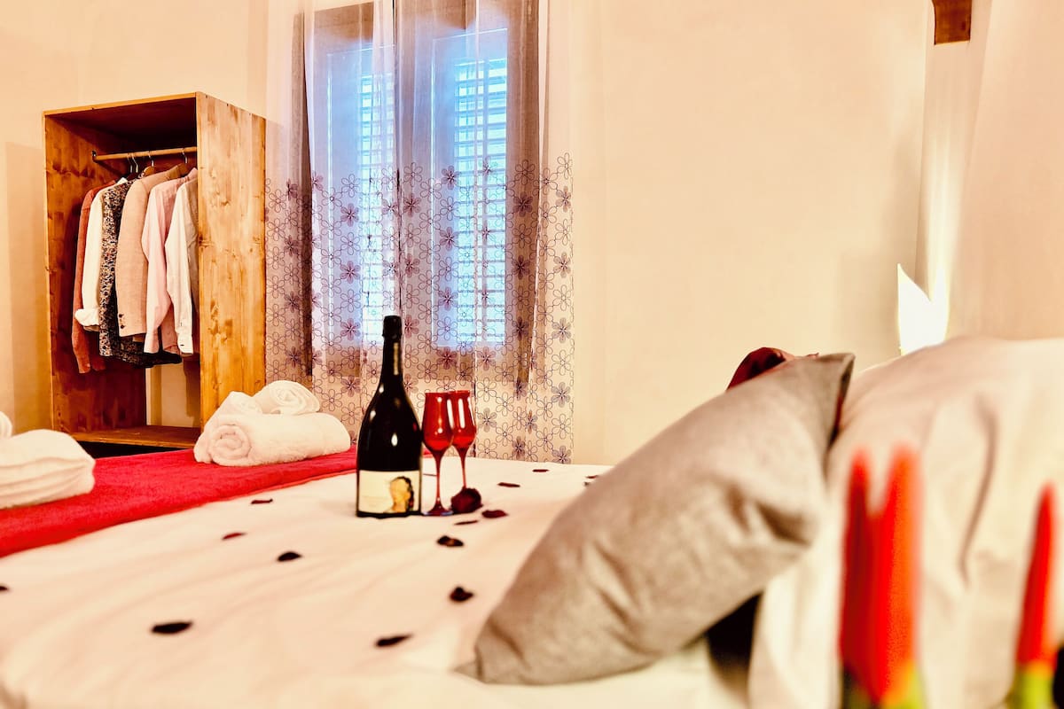 A hotel room with a bed, a wooden wardrobe, a bottle of wine, and two wine glasses.