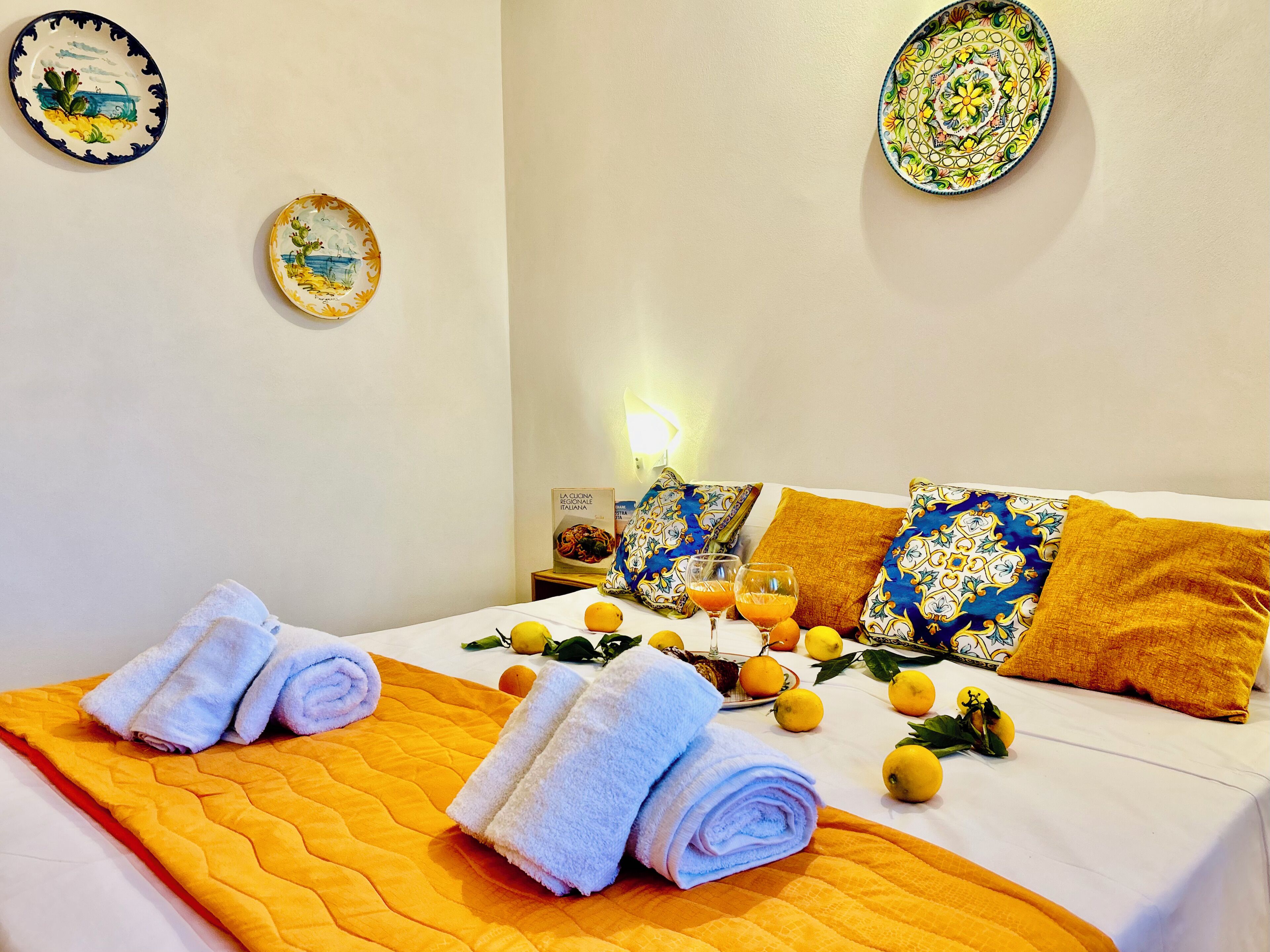 A neatly made bed with rolled towels, a yellow quilt, and decorative pillows.