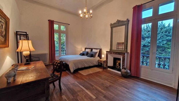 A bedroom with a bed, a desk, a chair, a fireplace, and large windows. - Le Manoir de la Belle Endormie (Valréas)