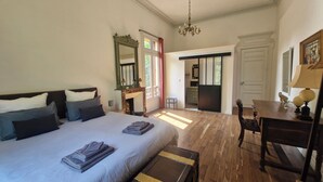 A bedroom with a large bed, a dresser, a desk, and a chair. There is a window with curtains, a mirror, and a chandelier. - Le Manoir de la Belle Endormie (Valréas)