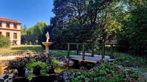 A garden with a pond, a statue, a bridge, and a building in the background. - Le Manoir de la Belle Endormie (Valréas)