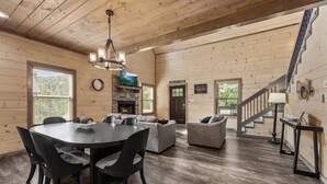 A spacious living area with a fireplace, a dining table with chairs, and a staircase. - Smoky Cove Retreat-Close to all the action! (Sevierville)