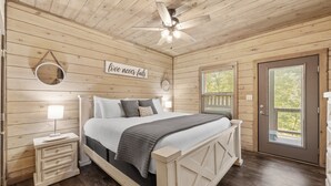 A wooden-paneled bedroom with a bed, bedside lamps, a ceiling fan, and a door with a view of the outdoors. - Smoky Cove Retreat-Close to all the action! (Sevierville)