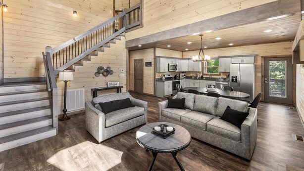 A spacious living area with a staircase, grey sofas, a round coffee table, and a kitchen in the background. - Smoky Cove Retreat-Close to all the action! (Sevierville)