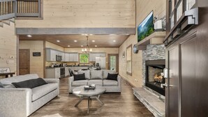 A spacious living room with a fireplace, grey sofas, and a kitchen in the background. - Smoky Cove Retreat-Close to all the action! (Sevierville)