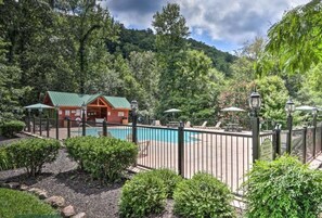 A cabin with a green roof, surrounded by a pool and a fenced patio area.