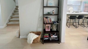 A modern interior with a staircase, a dark wooden bookshelf with books and decorative items, and a kitchen area with bar stools. - Luxury 3B house near Tec Hubs, High speed WiFi, Chef's Kitchen (San Jose)