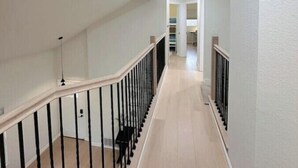 A spacious, well-lit hallway with a wooden floor and black railings, leading to a kitchen area. - Luxury 3B house near Tec Hubs, High speed WiFi, Chef's Kitchen (San Jose)