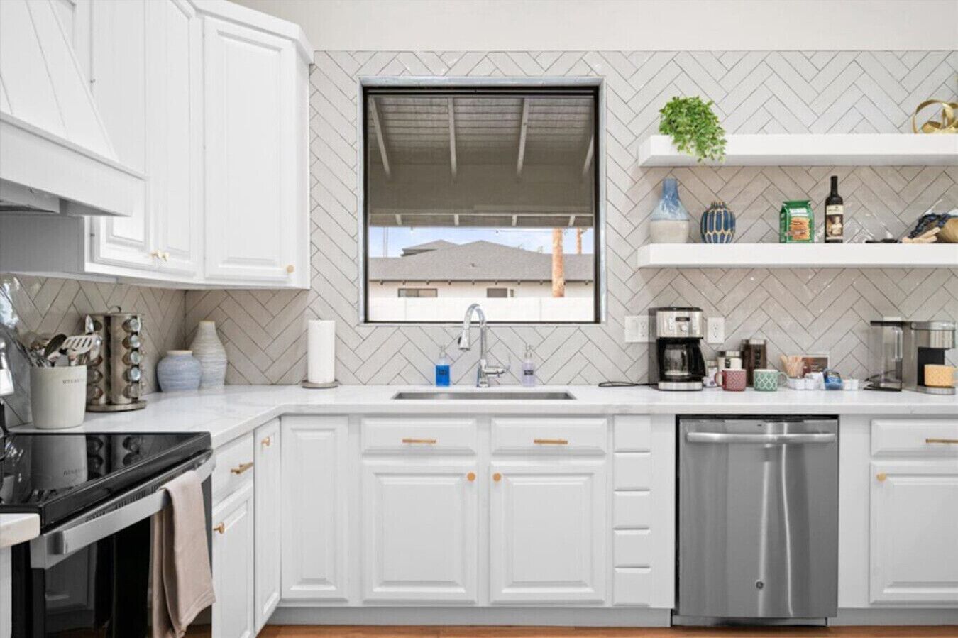 A modern kitchen with white cabinetry, a stainless steel dishwasher, and a window above the sink.