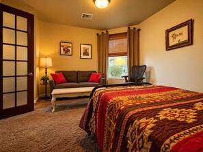 A hotel room with a bed, a sofa, a desk, and a chair. There is a window with curtains, a lamp, and framed pictures on the wall. - The Gem of The Preserve (Marana)
