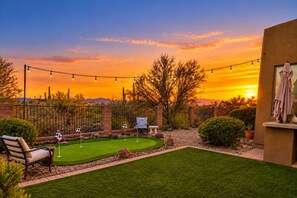 A backyard with a putting green, a patio table, and a chair. - The Gem of The Preserve (Marana)