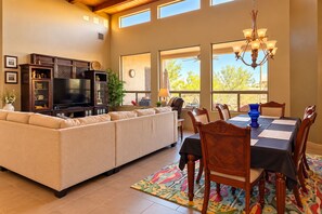 A spacious living room with a sectional sofa, a flat-screen TV, and a dining area with a table and chairs. - The Gem of The Preserve (Marana)
