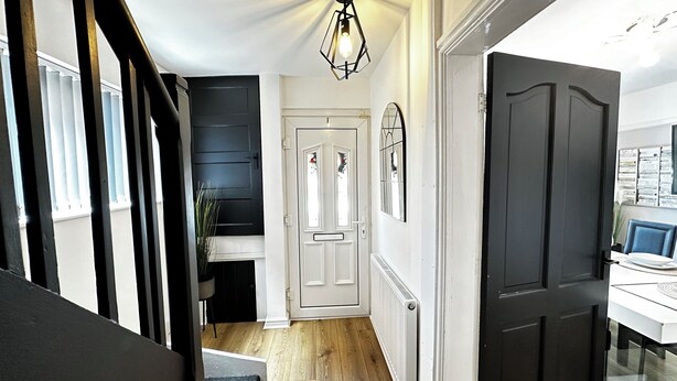 A modern interior with a staircase, a white door with glass panels, and a black door leading to a room with a blue chair and a table.