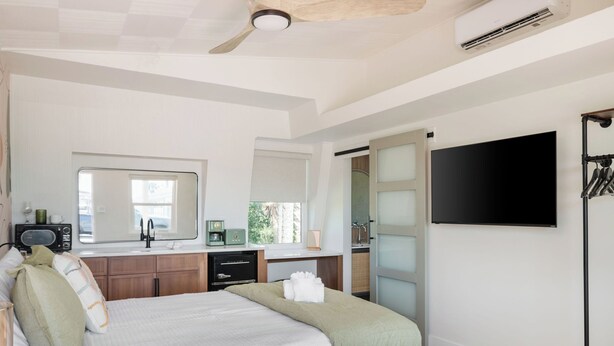 A modern bedroom with a bed, a flat-screen TV, a ceiling fan, and a window.