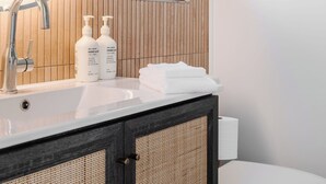 A bathroom with a round mirror, a modern faucet, two bottles of hand and body wash, a towel, and a makeup towel on a sink.