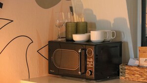 A microwave on a table with a box of coffee and a basket of bread.