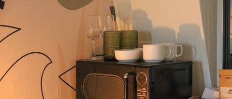 Un four à micro-ondes sur une table, à côté d’une boîte de café et d’un panier de pain.