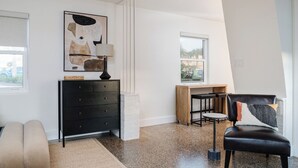 A modern room with a black leather chair, a wooden desk, and a black dresser. There is a window providing natural light and a view of the outside. - Aviles Double Full- 5 min walk to beach! (St. Augustine)
