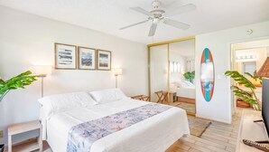 Hotellihuone, jossa on sänky, kattotuuletin, peili ja surffilaudan muotoinen koriste.