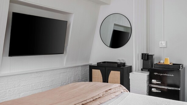 A bedroom with a bed, a TV mounted on the wall, a small cabinet, and a mirror. - The Ocean Queen Studio -5 min walk to beach! (St. Augustine)