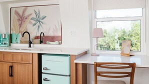 Een keuken met een wit aanrecht, een spoelbak, een blauwgroene koelkast, houten kastjes en een raam met uitzicht op groen.