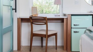 Una habitación con una silla de madera, un escritorio, un armario azul verdoso y una ventana con vista a follaje.