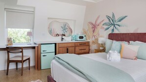 Un dormitorio con cama, escritorio, silla, una pequeña kitchenette y un mural en la pared.