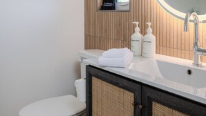 Un baño moderno con inodoro blanco, tocador con espejo y dos botellas de jabón corporal y loción.