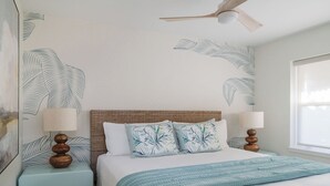Ein Schlafzimmer mit einem Bett, zwei Nachttischen, einem Deckenventilator und einem Fenster.