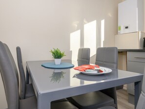 A modern dining area with a glass table, grey chairs, a small potted plant, and a plate with food items. - Lower Wortley 3 - Couples Haven with a Shared Kitchen - Pass the Keys (Leeds)