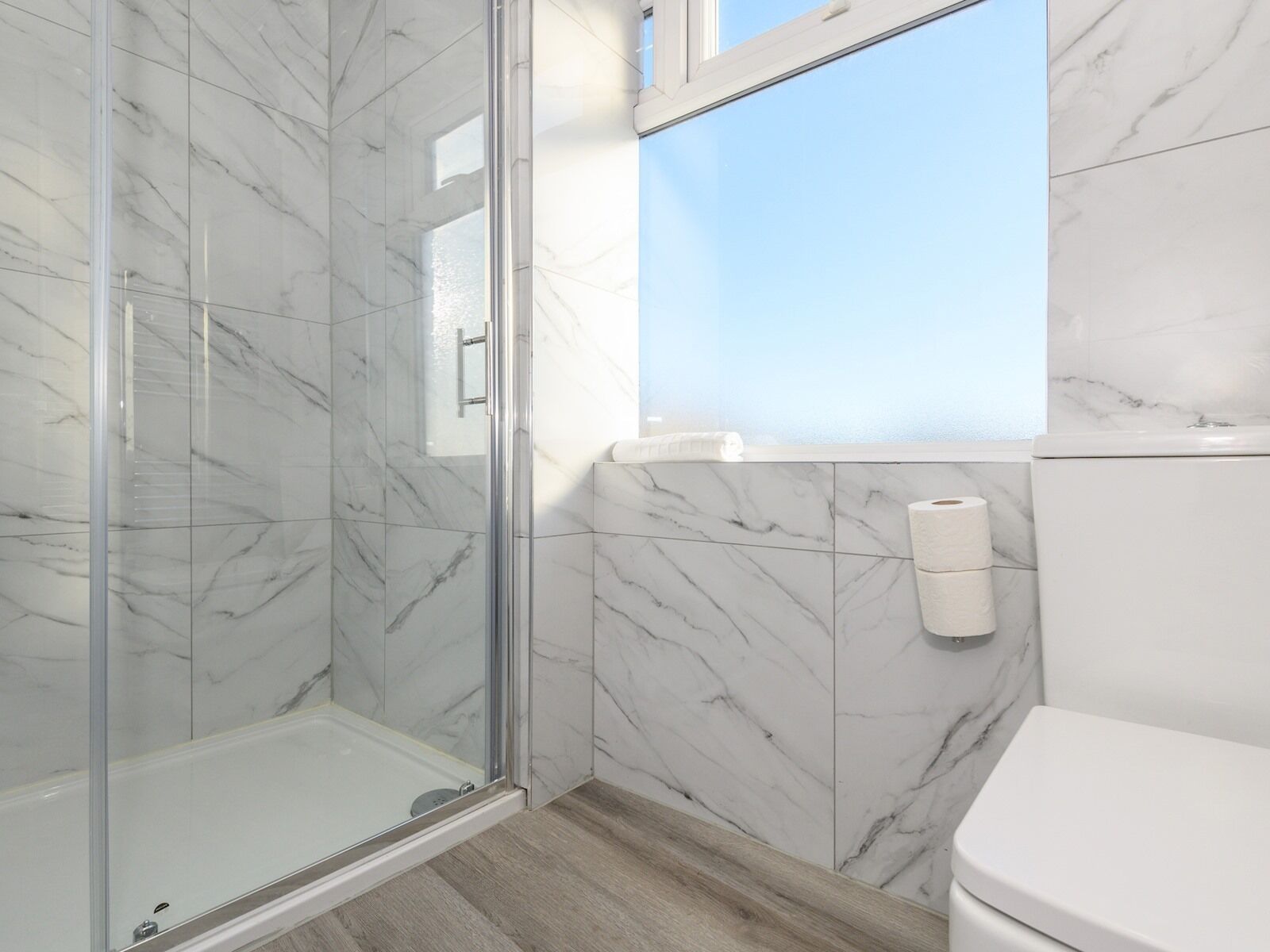 Een badkamer met een glazen douchecabine, marmeren wanden en een toilet.