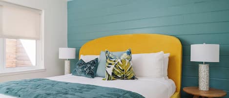 A bed with a teal headboard, white bedding, and decorative pillows. There are two bedside tables with lamps.