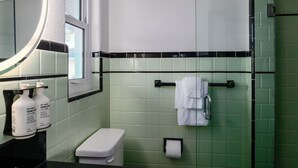 A bathroom with green tiles, a white toilet, a sink with hand soap, and a mirror. - The Vilano Queen Studio - 5 min walk to beach! (St. Augustine)