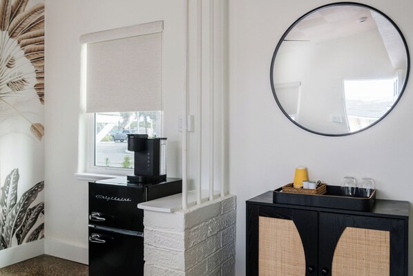A modern bathroom with a white vanity, a black cabinet with wicker baskets, and a round mirror.