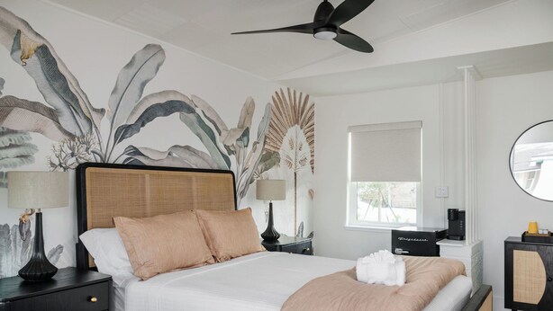A neatly arranged bedroom with a large bed, a ceiling fan, a window with blinds, and a wall-mounted mirror. - The Vilano Queen Studio - 5 min walk to beach! (St. Augustine)