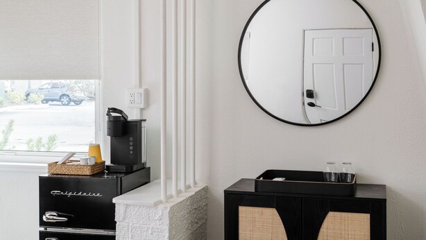 A modern hotel room with a fireplace, a coffee machine, a black console table with glasses, and a round mirror on the wall. - The Castillo Queen Studio -5 min walk to beach! (St. Augustine)