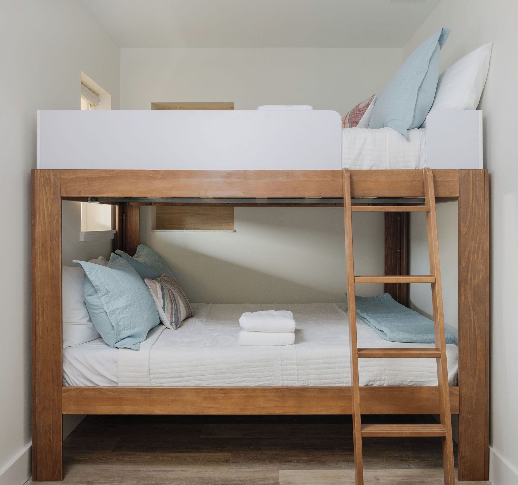 A bunk bed with a wooden frame, white bedding, and a ladder.