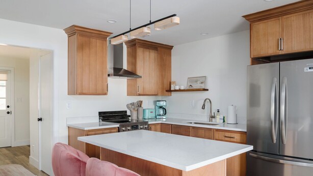 Een moderne keuken met houten kastjes, een roestvrijstalen koelkast, een koffiezetapparaat en een roze stoel.