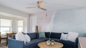 Een moderne woonkamer met een donkerblauwe hoekbank, een houten salontafel en een plafondventilator.