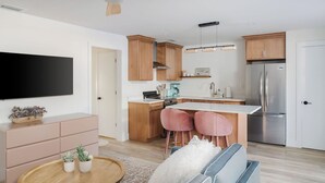 Een moderne keuken met houten kastjes, een roestvrijstalen koelkast, een flatscreen televisie en een eethoek met roze stoelen.
