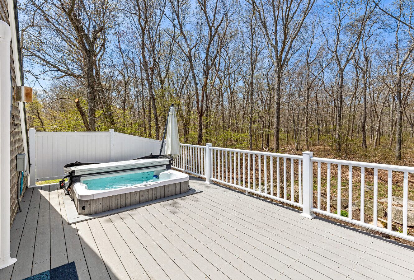 Une terrasse en bois avec un jacuzzi et une rambarde blanche.