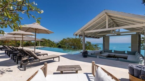A poolside area with lounge chairs, umbrellas, and a seating area overlooking a clear blue sky and ocean.