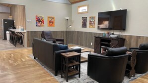 A modern living room with a sofa, chairs, a coffee table, and a TV. There is a kitchen area with a refrigerator and a dining table with chairs. - Spacious Convenient Downtown Cody Location (Cody)